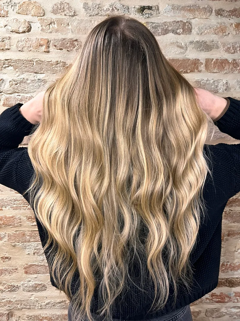 Capelli lunghissimi e mossi con schiariture bionde, visti da dietro davanti al muro di mattoni