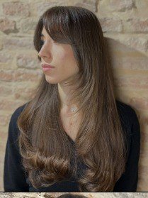 Profilo con frangia e capelli mossi, sfondo in mattoni